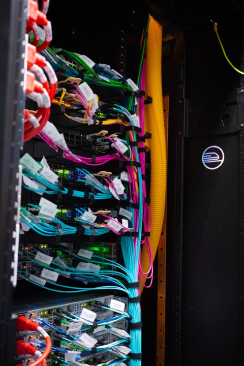 Open datacenter rack with neatly combed bundles of pink, teal and green fiber, Railway's logo on the door